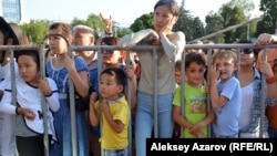 Молодежь, дети и взрослые стоят за ограждением у сцены во время мероприятия в Алматы.