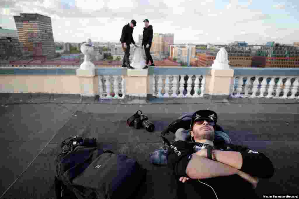 A member of "Rudex" rests as his teammates stand perched on the parapet of a Moscow roof.