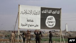 Ирак әскері ИМ-нен басып алған Хит қаласындағы ИМ туы мен ұрандары жазылған билборд астында тұр. Ирак, сәуір 2016 жыл.