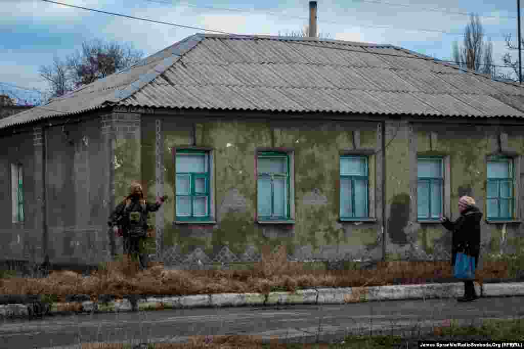 Жінка чекає, поки український солдат повідомить, чи прохід вулицею є безпечним.