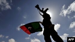 A Libyan opposition fighter waves the flag of the rebellion on a desert road some 30 kilometers from the eastern town of Brega on March 31.