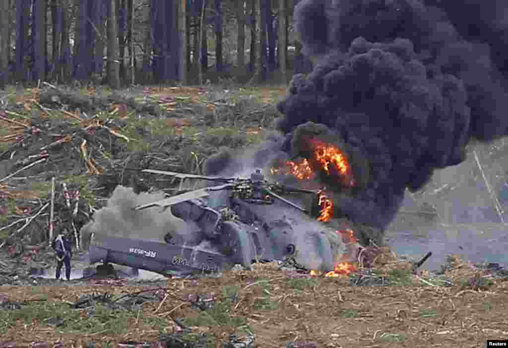 A pilot (left) stands near his burning Mi-28N from the Berkuty (Golden Eagles) helicopter display team after a crash during a military aviation competition at the Dubrovichi range near Ryazan, Russia. The other pilot was killed. (Reuters/Maxim Shemetov)&nbsp;