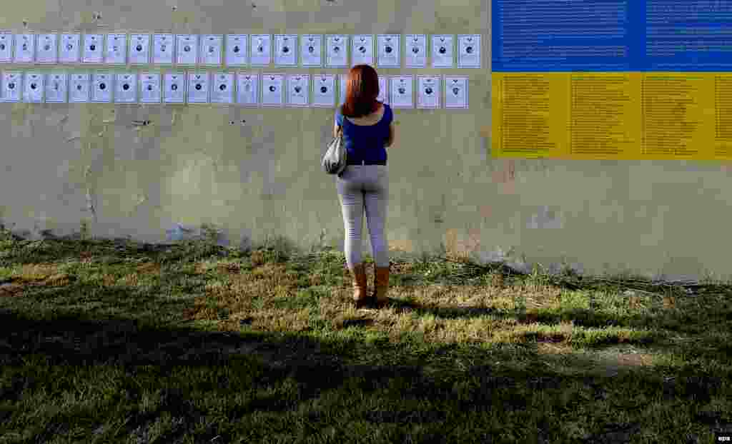 A woman looks at memorial cards on a wall near the symbolic graveyard identifying the Euromaidan dead.