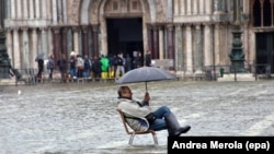 Турист сидит на стуле посреди воды в центре Венеции. Иллюстративное фото.