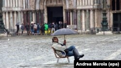 Сел басқан Венецияда жаңбыр астында отырған турист. Көрнекі сурет