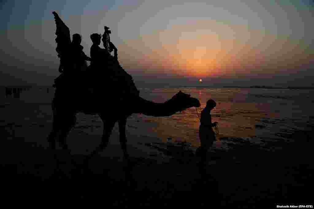 People ride a camel on a beach in Karachi, Pakistan. (epa-EFE/Shahzaib Akber)