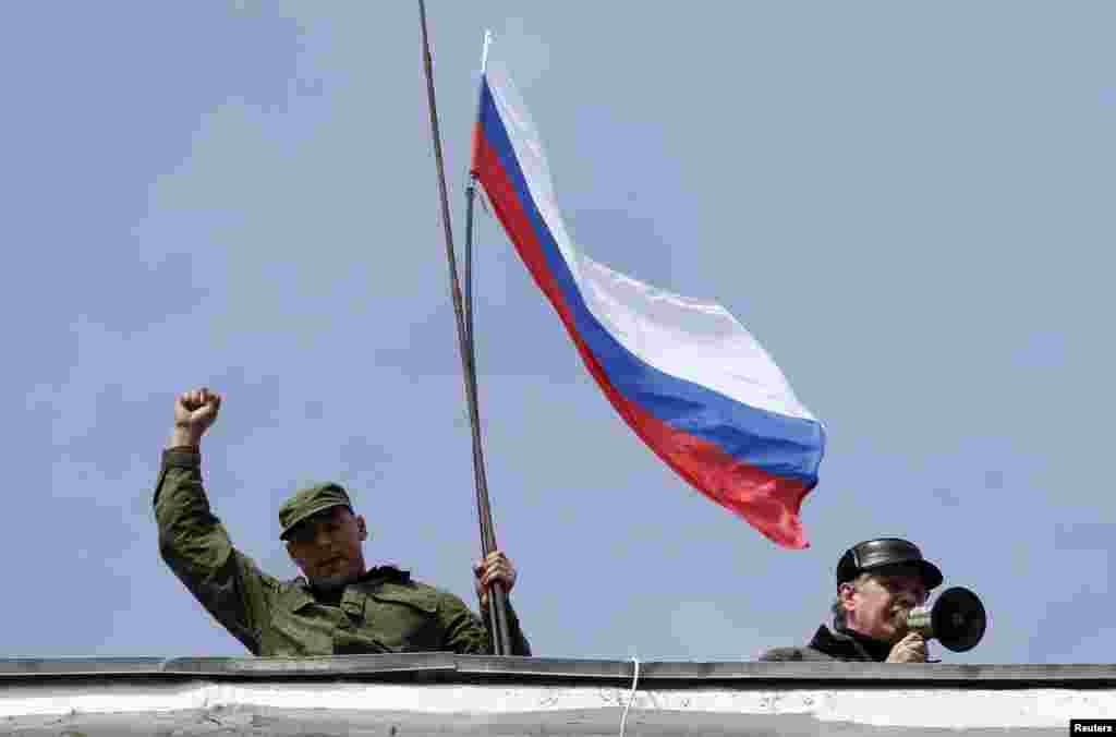 Ukraine -- A man holds a Russian flag on the roof of Ukrainian naval headquarters as another man addresses the crowd outside with a megaphone in Sevastopol, March 19, 2014