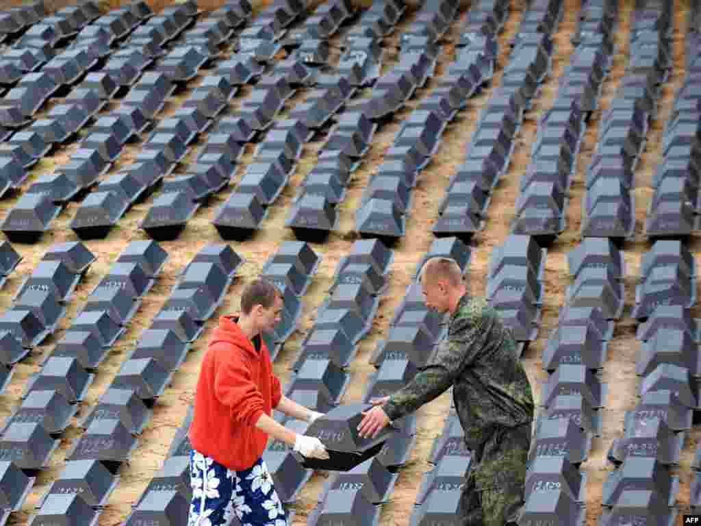 Two men put boxes into the grave during a reburial ceremony of a thousand remains of German soldiers killed during World War II at a cemetery near the town of Bobruisk, some 150 kilometers south of Minsk on August 11. Photo by Viktor Drachev for AFP