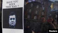 People look at a "Wanted" notice for fugitive President Victor Yanukovych, which was plastered on the window of a car used as barricade, near Kyiv's Independence Square on February 24