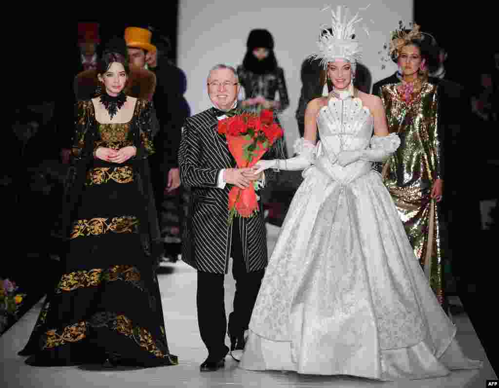 Russian fashion designer Slava Zaitsev (center) walks on stage surrounded by models.