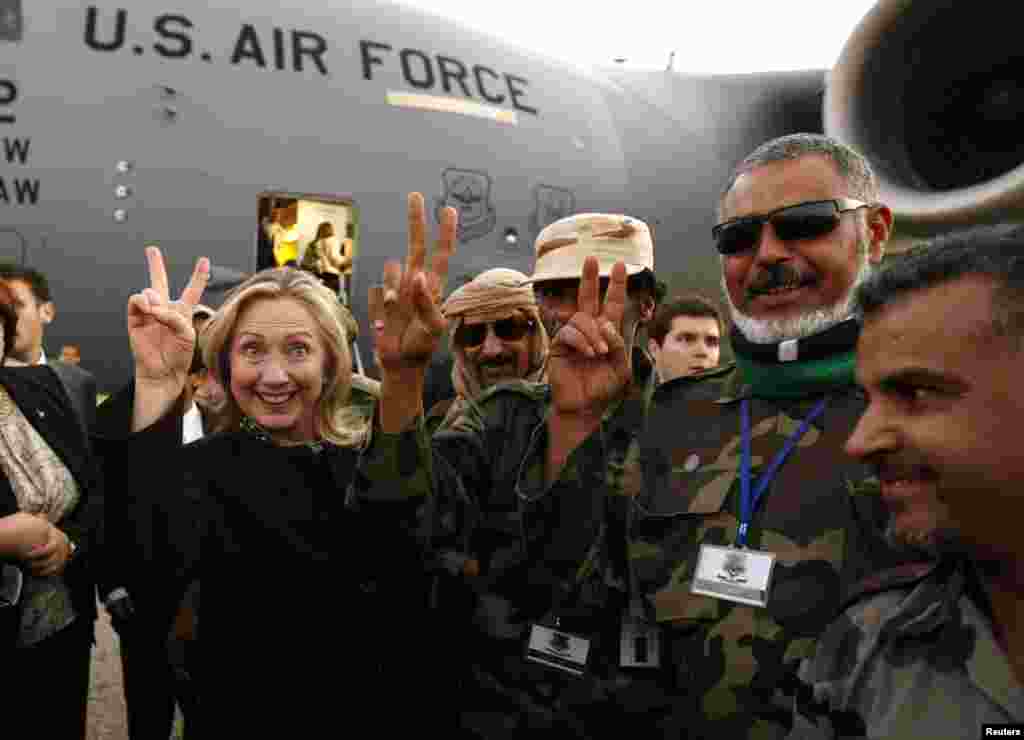 Мамлекеттик катчы Клинтон Триполиден узап бараткан маалда ливиялык аскерлер менен жеңиштин белгисин көрсөтүп сүрөткө түшүүдө. 18-октябрь, 2011.