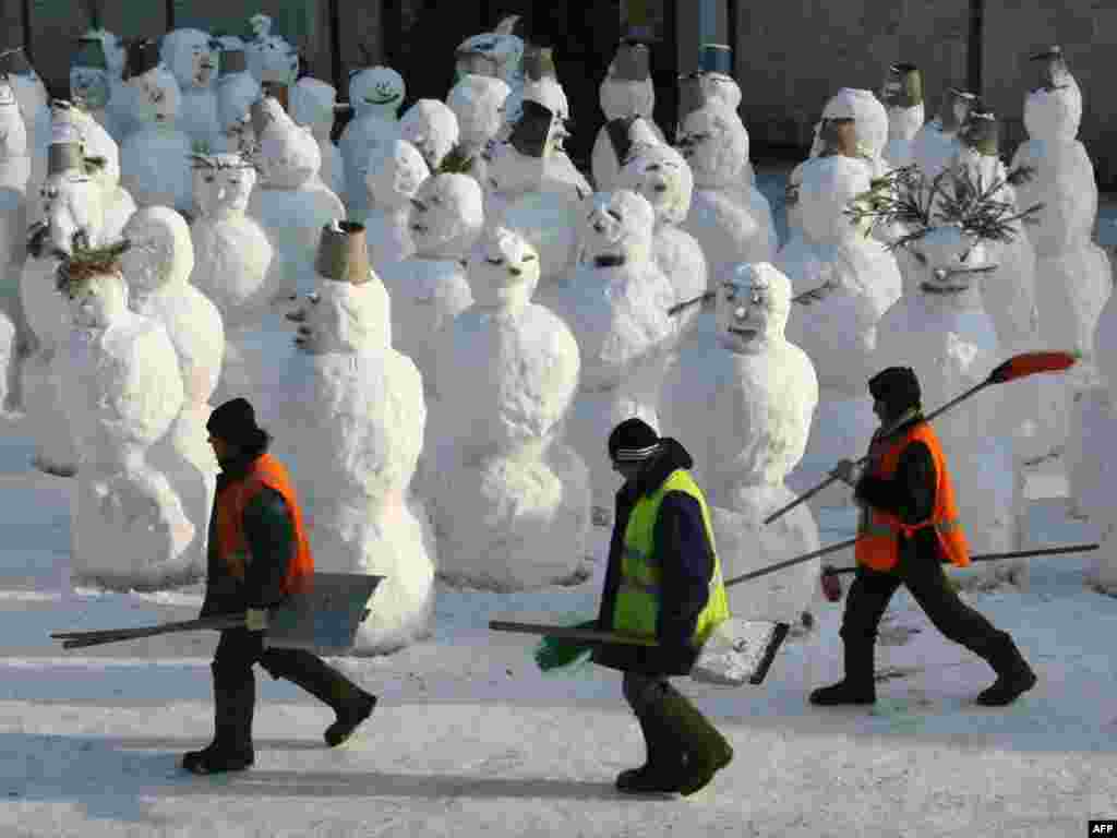 Migrant workers walk past a group of snowmen in Moscow. - Photo by Aleksei Sazonov for AFP