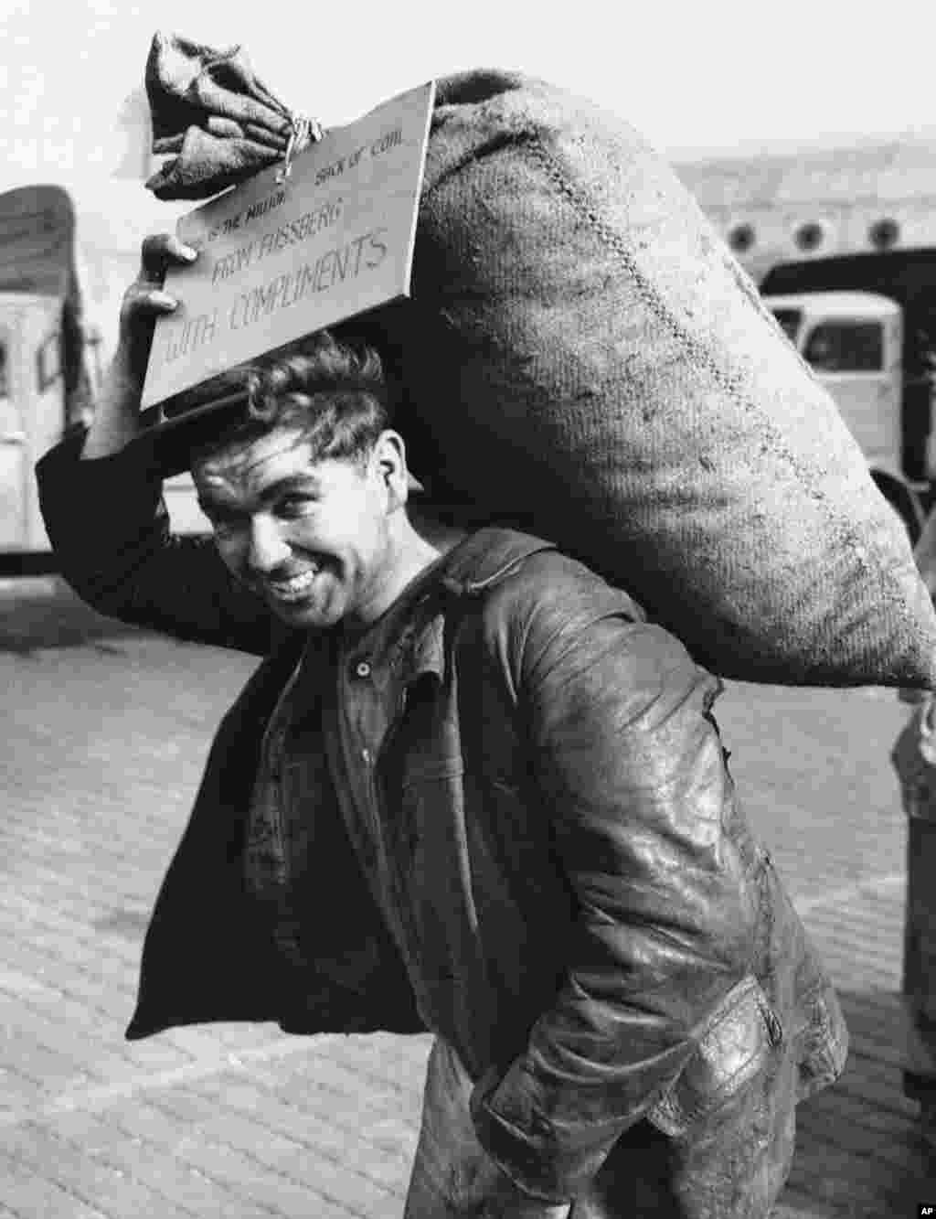 Немецкий рабочий несет миллионный доставленный в город мешок с углем, 20 сентября 1948 года. Надпись на &quot;открытке&quot; гласит: &quot;С наилучшими пожеланиями из Фассберга&quot;. База в Фассберге, Нижняя Саксония, использовалась британскими ВВС для операции, которую окрестили &quot;Летающие угольные вагонетки&quot;.&nbsp;&nbsp;