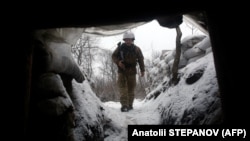 Украински войник влиза в покрития от сняг окоп на бойното поле