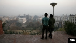 A couple stands at a viewpoint overlooking Tehran, which is covered in smog.