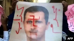 An image grab taken from a video uploaded on YouTube allegedly shows antiregime protesters holding a defaced poster of President Bashar al-Assad in the Qadam neighborhood of Damascus in early November.