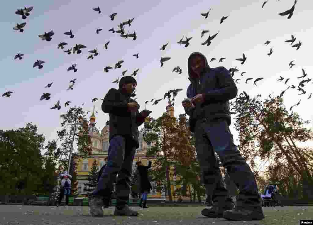 Njerëzit duke ushqyer pëllumbat para një katedrale në një park në Almati, Kazakistan.