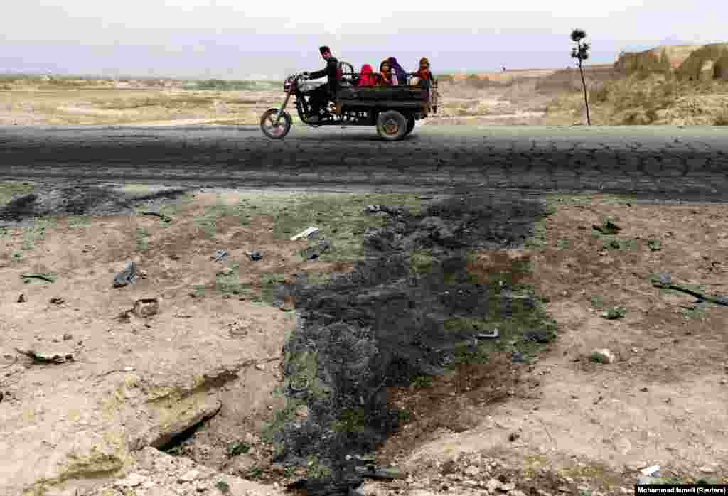 An Afghan family ride on a bike past the site of a car bomb attack near Bagram air base on April 9. (Reuters/Mohammad Ismail)&nbsp;