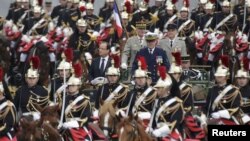 French President Francois Hollande (center left) stands to attention in a command car as he reviews troops on the Champs-Elysees in Paris at the start of the traditional Bastille Day military parade. 