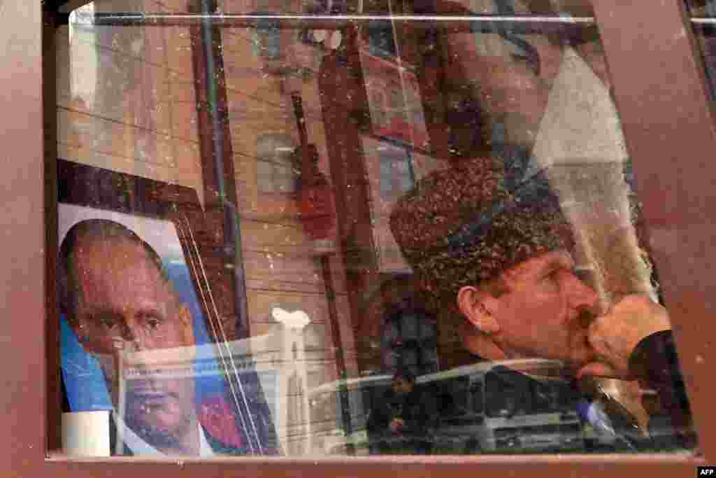 A street vendor waits for customers while sitting next to a portrait of Russian President Vladimir Putin at a kiosk in central Moscow. (AFP/Kirill Kudryavtsev)