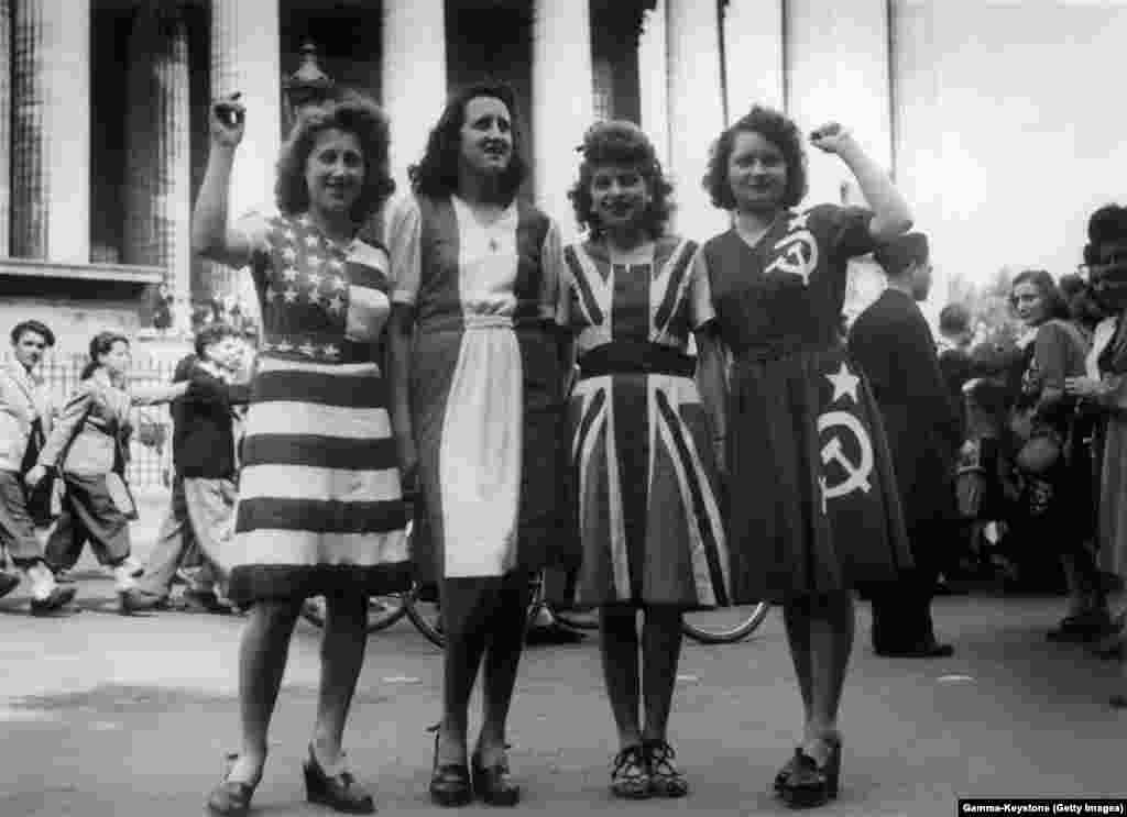 Femei îmbrăcate cu steagurile Statelor Unite ale Americii, Franței, Marii Britanii și Uniunii Sovietice la sărbătorirea Zilei Victoriei în centrul Parisului.