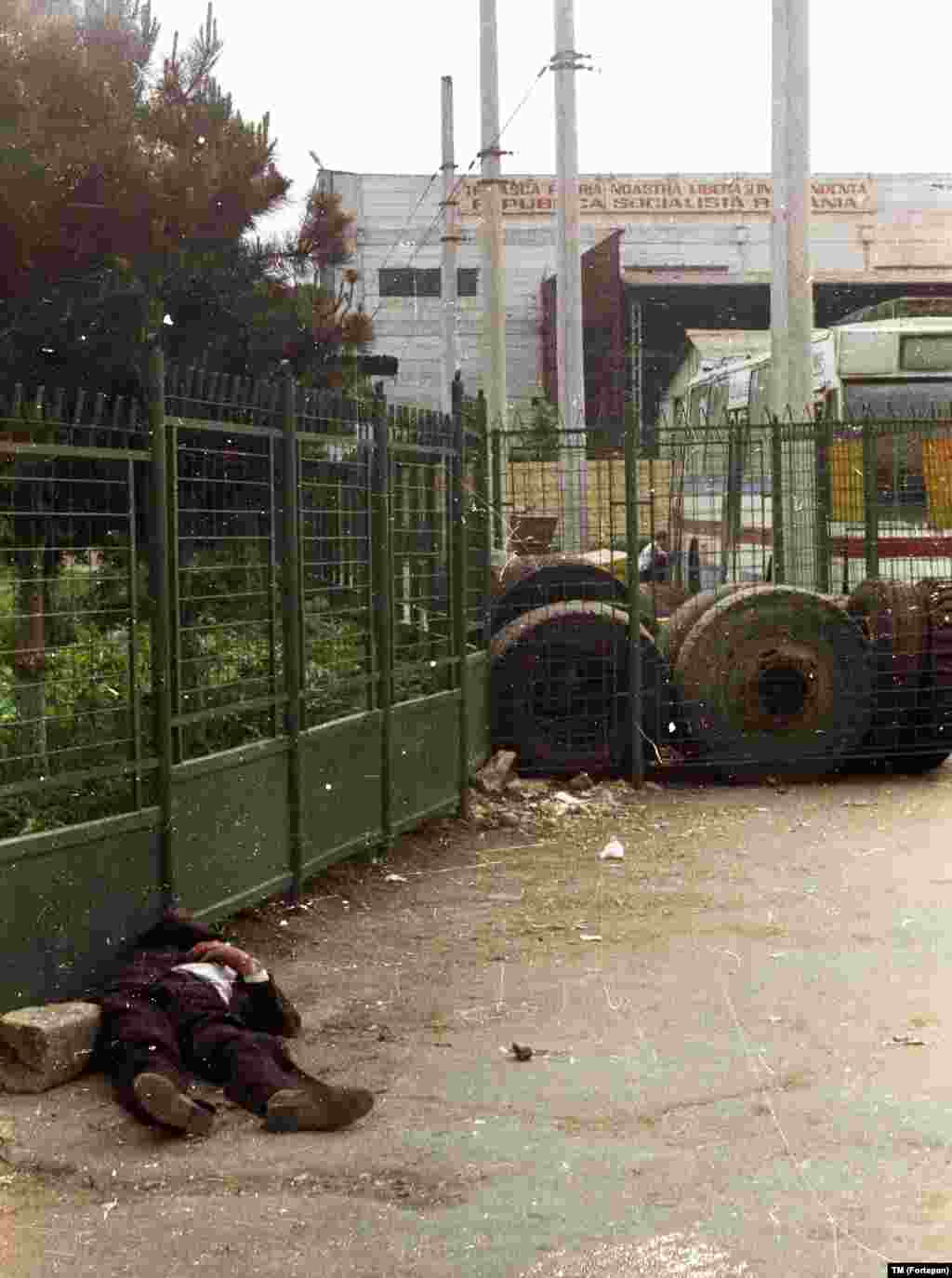 Спящий (вероятно, пьяный) человек у ворот фабрики, над которой виден лозунг &quot;Да здравствует наша свободная и независимая родина &ndash; Социалистическая Республика Румыния!&quot;.&nbsp; &nbsp;