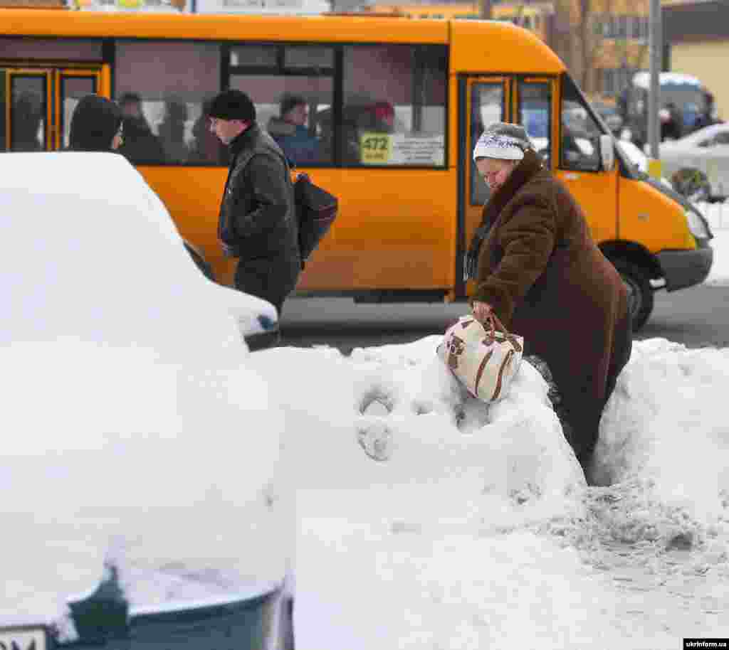 У столиці тривають роботи із прибирання снігу на дорогах, тротуарах, зупинках. На фото: жінка проходить через купу снігу на узбіччі дороги, Київ, 11 січня 2016 року.&nbsp;​