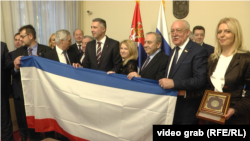 Natalija Poklonskaya, deputete e Dumës Shtetërore Ruse, me Boshko Obradoviqin, themeluesin dhe udhëheqësin e Dverit, tregon flamurin e Krimesë të aneksuar nga Rusia, në Asamblenë Kombëtare të Republikës së Serbisë, më 2019.