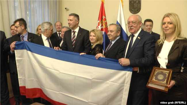 Natalija Poklonskaya, deputete e Dumës Shtetërore Ruse, me Boshko Obradoviqin, themeluesin dhe udhëheqësin e Dverit, tregon flamurin e Krimesë të aneksuar nga Rusia, në Asamblenë Kombëtare të Republikës së Serbisë, më 2019.
