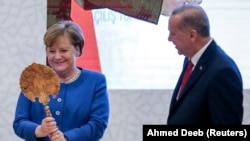 Angela Merkel (solda) bu ilin yanvarında İstanbulda Türkiyə-Almaniya Universitetinin yeni şəhərciyinin açılışında Türkiyə Prezidenti Recep Tayyip Erdoğanın hədiyyəsini qəbul edir 