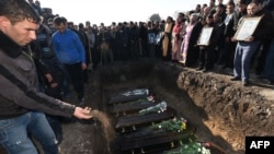 Armenia -- A man throws a handful of soil on coffins of victims during a funeral ceremony held for the six members of the same family allegedly killed by Russian soldier Valery Permyakov in the city of Gyumri, at the city's local cemetery, January 15, 2015