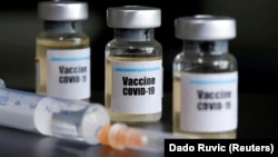 Маленькие бутылочки с наклейкой «Vaccine COVID-19» и медицинский шприц. Иллюстративное фото.