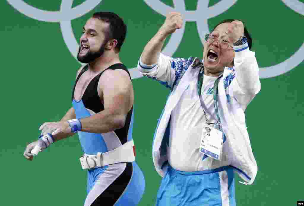 Nijat Rahimov (L) of Kazakhstan celebrates with a member of the coaching staff after setting a new world record and winning the gold medal in the men's weightlifting 77-kilogram category.