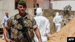 A Lebanese Army soldier walks past investigators inspecting the scene where two drones came down in the vicinity of a media center of the Shi'ite Hezballah, south of the capital Beirut on August 25.