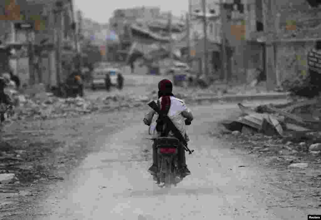 A man drives a motorcycle while carrying his weapon near damaged buildings in the northern Syrian town of Al-Bab. (Reuters/Khalil Ashawi)