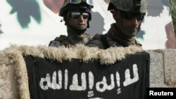 Soldiers look at the flag of Al-Qaeda militants on the wall of a house that used to be a weapons cache in western Baghdad. (file photo)