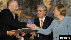 Мұхаммед пайғамбарға карикатура салған даниялық суретші Курт Вестергаардты (сол жақта) Германия канцлері Ангела Меркель (оң жақта) жүлдесімен құттықтап жатыр. Германия, Потсдам, 8 қыркүйек 2010 жыл.
