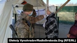 Пограничник проверяет температуру у женщины, пересекающий линию разграничения, КПВВ Станица Луганская