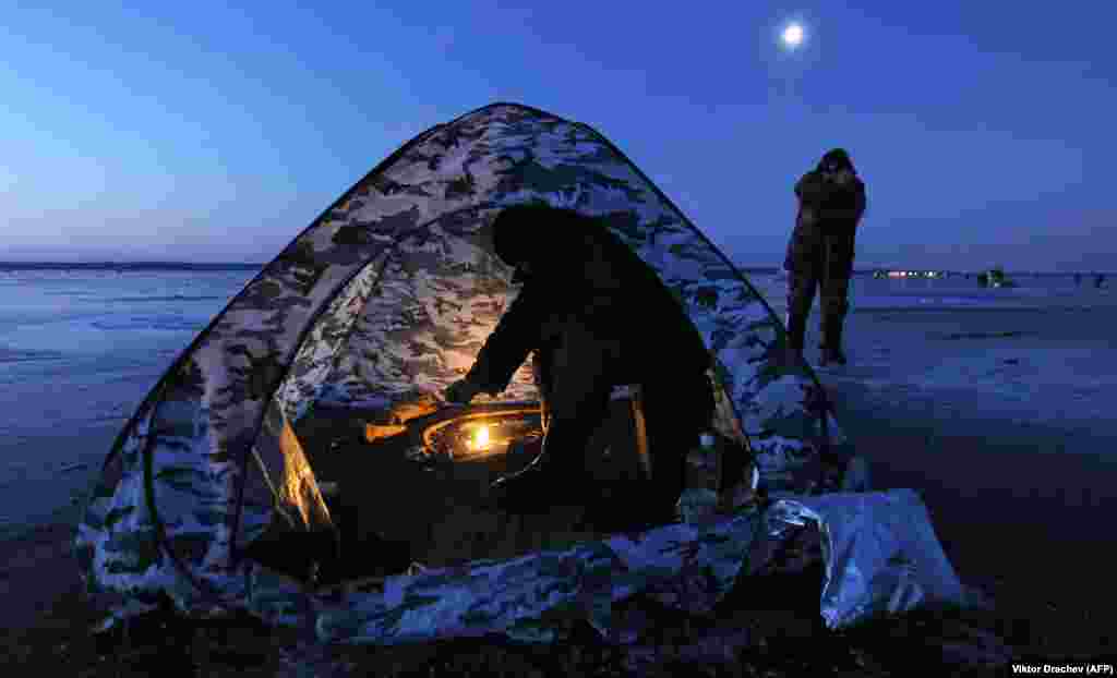 A man sits in a tent while ice fishing at sunrise on Lake Vileika, some 130 kilometers north of the Belarusian capital, Minsk. (AFP/Viktor Drachev)