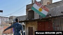یکی از نیروهای وفادار به دولت عراق در حال پایین کشیدن پرچم اقلیم کردستان از یکی از ساختمان‌های کرکوک