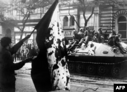 Мъж развява опръскано с кръв чехословашко знаме, докато бронирана машина превозва съветски войски през Прага.