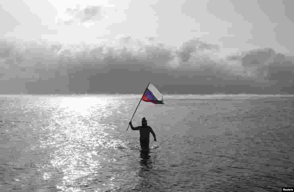 A man holds a Russian national flag while walking out of the Black Sea, as fans of winter swimming gathered on a beach on Orthodox Christmas in the Crimean port of Yevpatoriya. (Reuters/Pavel Rebrov)