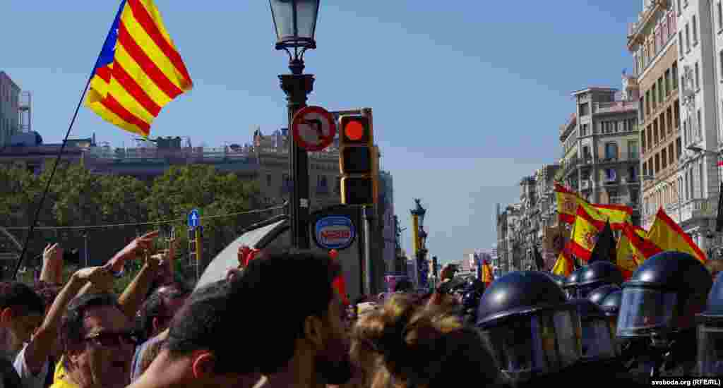 Зьлева сьцяг каталёнскіх незалежнікаў, справа ідзе шэсьце ў патрымку нацыянальнай паліцыі пераважна пад гішпанскімі сьцягамі, а паміж імі кардон мясцовай каталёнскай паліцыі.&nbsp;