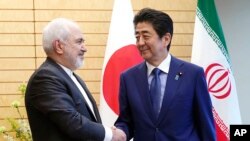 Iranian Foreign Minister Mohammad Javad Zarif, left, and Japanese Prime Minister Shinzo Abe, right, shake hands at Abe's official residence in Tokyo Thursday, May 16, 2019. (AP Photo/Eugene Hoshiko, Pool)