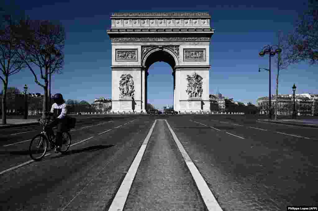 France - A man rides his bicycle past the Arc de Triumph in Paris, 23Mar2020