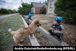 Vova, 7, and his little brother Stepan play with a dog in Luhanske.