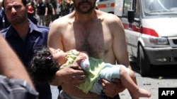 Syria -- A man carries a wounded girl next to Red Crescent ambulances following an explosion that targeted a military bus near Qudssaya, a neighborhood of Damascus, 08Jun2012