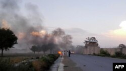 Afghan men watch the aftermath of a suicide car bomb attack at Camp Chapman in Khost Province on July 12.