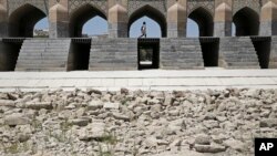 In this Tuesday, July 10, 2018 photo, a woman walks on the 400-year-old Si-o-seh Pol bridge, named for its 33 arches, that now spans a dried up Zayandeh Roud river, in Isfahan, Iran. Farmers in central Iran are increasingly turning to protests, pleading t