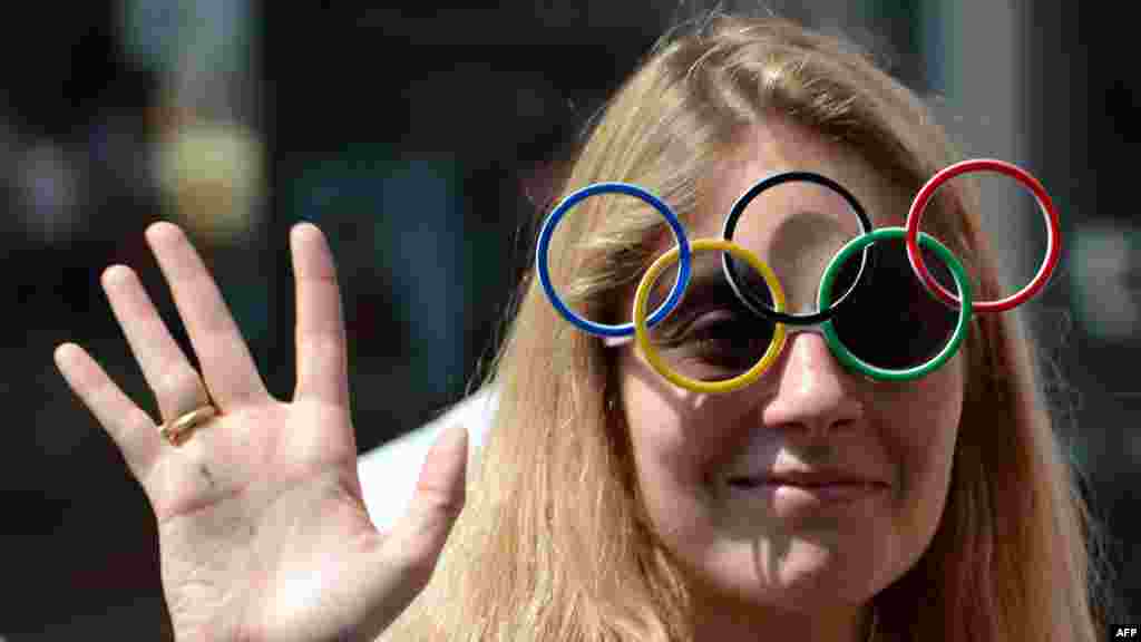 A woman wearing sunglasses featuring the Olympic rings cheers during the torch relay on July 26. (AFP/Miguel Medina)